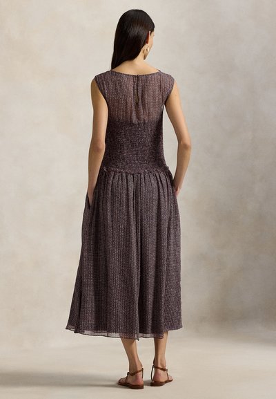 Knee-length, sleeveless dress in textured burgundy fabric with a fitted bodice, loose skirt, and back button detail. Sandals complete the look.