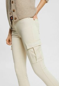Beige cargobroek met zijzakken, aansluitend ontwerp en een gladde textuur. Gecombineerd met een lichtbruine gebreide cardigan.