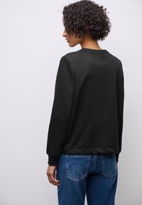 Sudadera negra de manga larga y cuello redondo con puños acanalados. Combinada con unos vaqueros rectos de pierna clara y desteñida. Textura suave.