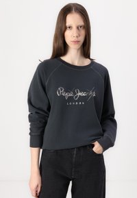 Felpa grigia scura con polsini e collo a coste. Presenta il logo "Pepe Jeans London" in bianco e argento. Indossata sopra dei pantaloni neri.