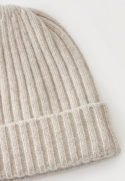 Bonnet en laine beige tricoté avec un revers plié, montrant un motif côtelé vertical et une texture douce sur fond blanc.