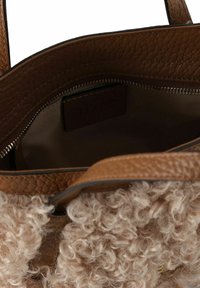 Bolso de mano de piel marrón con forro de piel de pelo beige rizado. El interior cuenta con un zipper y una pequeña etiqueta. Diseño estructurado con dos asas.