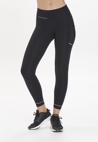 Svarta leggings i elastiskt material med hög midja, som har sidofickor och vit kontrastsöm vid fållarna.