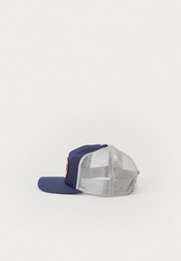 Gorra de béisbol azul marino con visera curva y parte trasera de malla. Presenta un parche circular de logo en rojo y negro en el lateral.