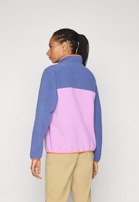 Fleece jacket with a purple upper and pink lower section. Features an orange zipper and trim. Smooth texture with a high collar.