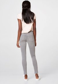 Jean skinny gris à la texture lisse, avec des poches arrière et une coupe ajustée, associé à une chemise à manches courtes rose pâle.