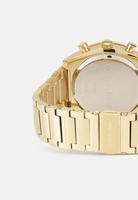 Gold stainless steel watch with a polished band, featuring a rectangular case, two pushers, and a smooth rear surface.