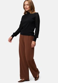 Pull noir avec des manches côtelées, associé à un pantalon large marron. La tenue présente une coupe décontractée et des textures douces.