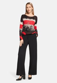 Czarna i czerwona wzorzysta bluzka z długim rękawem i okrągłym dekoltem, w połączeniu z czarnymi spodniami o szerokich nogawkach i błyszczącymi czarnymi szpilkami.
