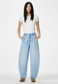 Hele sinised kõrge vöökohaga teksad, mis on valmistatud teksariidest, lahtise lõikega, suurte küljetaskutega ja pehme pleekimisega reite piirkonnas.