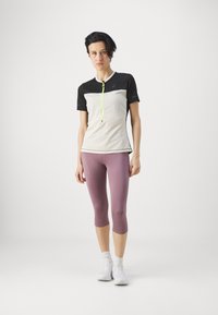 Top atlético ligero de manga corta en gris con detalles en negro y una cremallera neón. Combinado con leggings capri en lavanda. Zapatillas blancas.