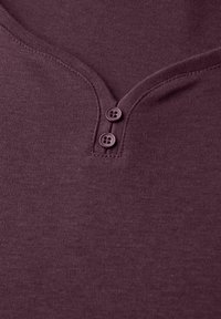 V-hals T-shirt in diepe bordeaux, gemaakt van zachte katoen, met twee donkere knopen en subtiele stikdetails langs de halslijn.