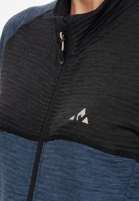 Sort og blå zip-up jakke med teksturerede stoffer. Har en høj krave, en sølvlynlås og et trekantet logo på brystet.