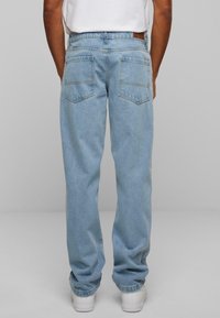Lys blå denimjeans med avslappet passform, fem lommer og synlige sømmer. Bena er lett tilspisset og bæres med hvite sneakers.