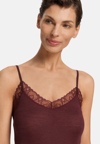 Burgunderfärgad linne med spetsdetaljer vid halsen, tunna axelband och en ribbad textur. Mjukt tyg med eleganta accenter.