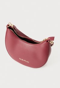 Burgundi nahkakäsilaukku, jossa on pyöreä, kuun muotoinen design, varustettuna vetoketjulla ja kultaisilla yksityiskohdilla. "VALENTINO" -logo kullassa edessä.