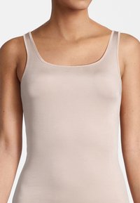 Canotta beige chiaro con scollatura quadrata e spalline sottili, realizzata in materiale liscio e elastico, aderente al corpo.
