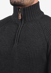 Maglione nero lavorato a maglia con collo alto a coste e chiusura a mezza cerniera. Presenta un dettaglio in pelle sulla cerniera e tessuto testurizzato.