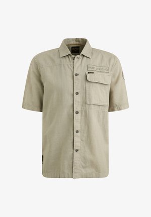 Košela s krátkym rukávom vo svetlo khaki farbe vyrobená z tkaného materiálu. Má zapínanie na gombíky, náprsné vrecko a vyšitú značku na ľavej strane.