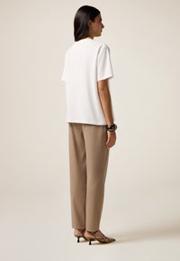 Witte t-shirt met korte mouwen, gecombineerd met losse, beige broek en gestreepte hakken, met een gladde textuur en een relaxte pasvorm.