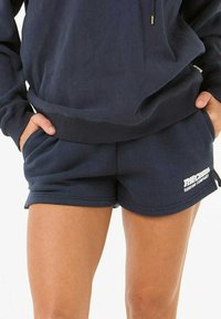 Marineblauwe sweatschoenen gemaakt van zachte stof, met een elastische tailleband, twee zijzakken en een logo in het wit gedrukt aan de zijkant.