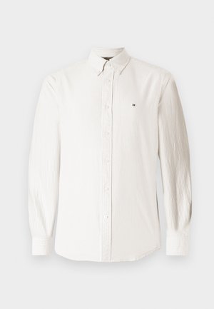 Camicia bianca a maniche lunghe con bottoni, realizzata in tessuto testurizzato con sottili righe verticali e un piccolo logo sul lato sinistro del petto.