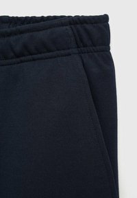 Mørkeblå sweatpants med elastisk talje. Har glat, tekstureret stof og sidelommer. Materialet ser åndbart og strækbart ud.