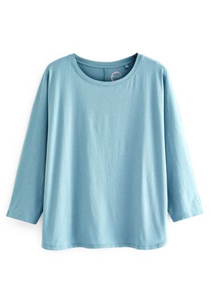 Camicia azzurro chiaro a maniche lunghe con scollo rotondo, vestibilità ampia e design semplice e lineare su sfondo bianco.