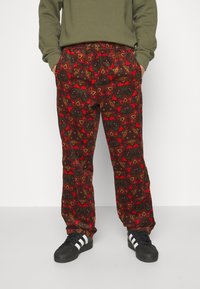 Röda mönstrade byxor med blommönster, elastisk midja och fickor, tillsammans med svarta skor med vita ränder.