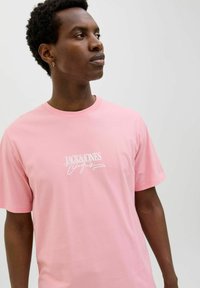 Šviesiai rožinė medvilninė marškinėliai su "JACK&JONES" brydė balta raš''meniu. Trumpomis rankovėmis, apvaliu iškirpimu ir įprastu pritaikymu.
