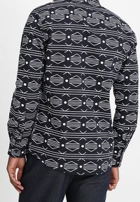 Zwarte longsleeve shirt met wit geometrisch patroon, met ontwerp van diamanten en cirkels. Gemaakt van stof, met een kraag en knoopsluiting.