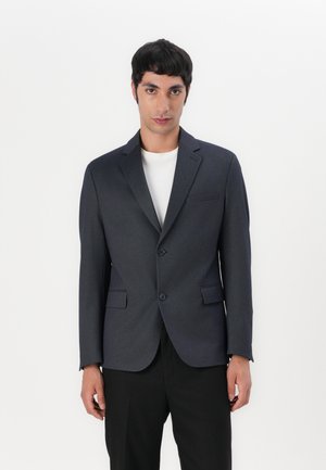 Dark blue blazer made of textured fabric, featuring a notched lapel, two front pockets, and a single-button closure. Paired with a white shirt.