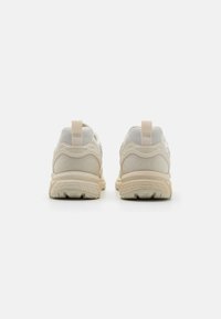 Beige athletic shoes with a mesh and textured material, featuring a padded collar and heel tab, and a patterned rubber outsole.