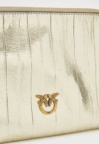 Clutch metallica dorata con una finitura testurizzata e stropicciata. Presenta una chiusura decorativa con due uccelli e un dettaglio ad anello circolare.