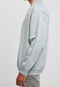 Světle modrý svetr s kulatým výstřihem, ribbovanými manžetami a lemem. Hladká textura, mírně volný střih a jemné detaily šití.