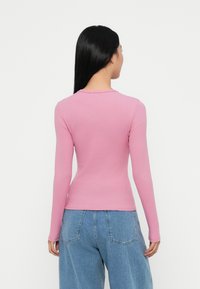 Long-sleeve pink shirt in ribbed fabric with a fitted shape. Paired with loose-fitting light blue denim jeans, showcasing a casual look.
