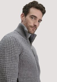 Grauer Strickpullover mit hohem Kragen und halbem Reißverschluss. Strukturiertes Muster mit gemütlichem Aussehen. Verfügt über einen gerippten Kragen und Ärmel.