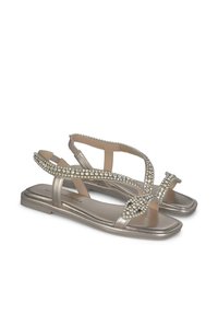 Sandali metallici dorati con cinturini trasparenti, adornati con strass trasparenti lungo i lati e una suola piatta per un facile utilizzo.