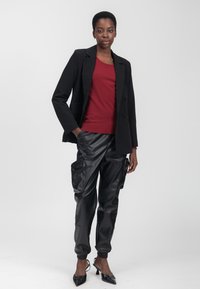 Blazer nero su misura sopra un maglione bordeaux, abbinato a pantaloni cargo in finta pelle nera con tasche laterali e polsini a sigaretta, completato da décolleté nere a punta.