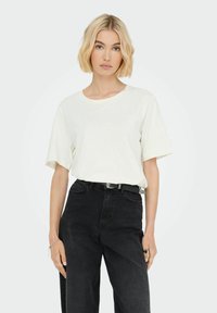 Hvid kortærmet T-shirt med rund hals, parret med højtaljede sorte jeans, der har et bælte med en blank spænde.