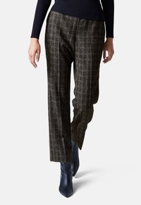 Hoge taille, wijde broek in gestructureerde zwarte stof met een ruitpatroon. Draagt een aansluitend zwart topje en puntige navy enkellaarzen.