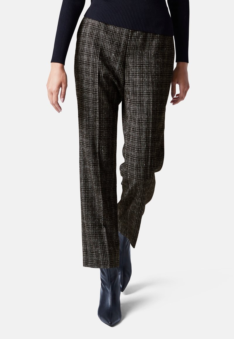 Hoge taille, wijde broek in gestructureerde zwarte stof met een ruitpatroon. Draagt een aansluitend zwart topje en puntige navy enkellaarzen.