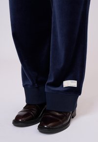 Marineblauwe fluwelen sweatpants met geribde boorden, voorzien van een label aan de zoom. Gecombineerd met gepolijste bruine schoenen die een klassiek ontwerp tonen.