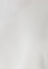 Bela, gladka tkanina z mehko teksturo. Nežen, enakomeren odtenek brez vidnih vzorcev ali kovinskih detajlov.