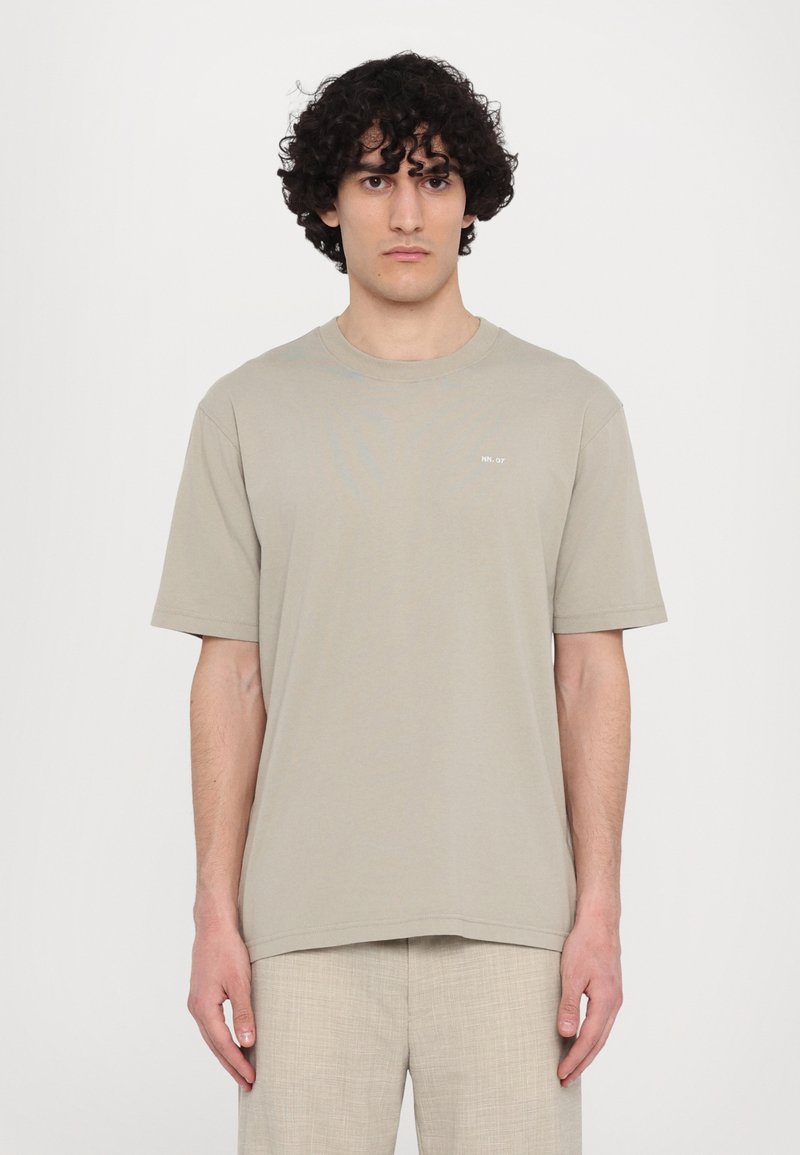 Beige katoenen t-shirt met korte mouwen, ronde hals en een klein gedrukt detail op de borst. Glad textuur, ontspannen pasvorm.