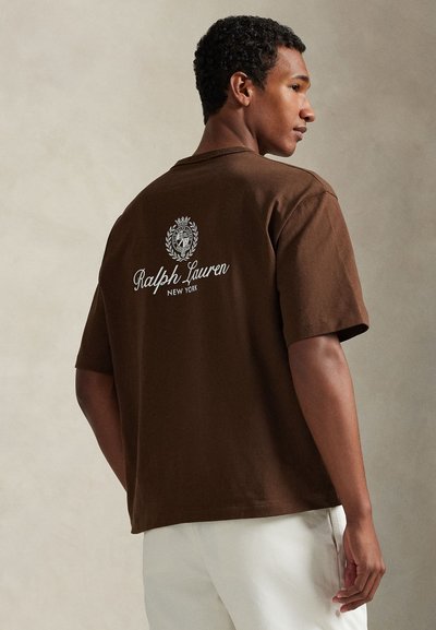 Καφέ βαμβακερό t-shirt με άνετη εφαρμογή, κοντά μανίκια και εκτύπωση λογότυπου στην πλάτη με τα λόγια "Ralph Lauren" και διακοσμητικά στοιχεία.