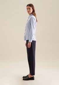 Lichtblauwe overhemdd met kraag, lange mouwen en een relaxte pasvorm, gecombineerd met donkerblauwe gesneden broek en zwarte instappers.