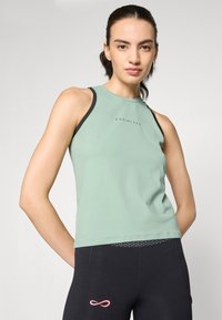 Light green athletic tank top with a high neckline, black trim, and “ENDLESS” logo in the center. Paired with black leggings featuring a pink accent.