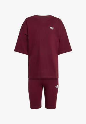 Weinrotes oversized kurzärmeliges Oberteil und passende knielange Shorts mit kleinen weißen Adidas Trefoil-Logos auf Brust und Oberschenkel.