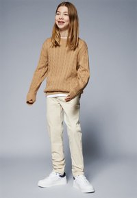 Maglione beige a tricot, pantaloni crema e sneakers bianche con dettagli blu navy. L'outfit presenta un tessuto lavorato a maglia e una vestibilità rilassata.